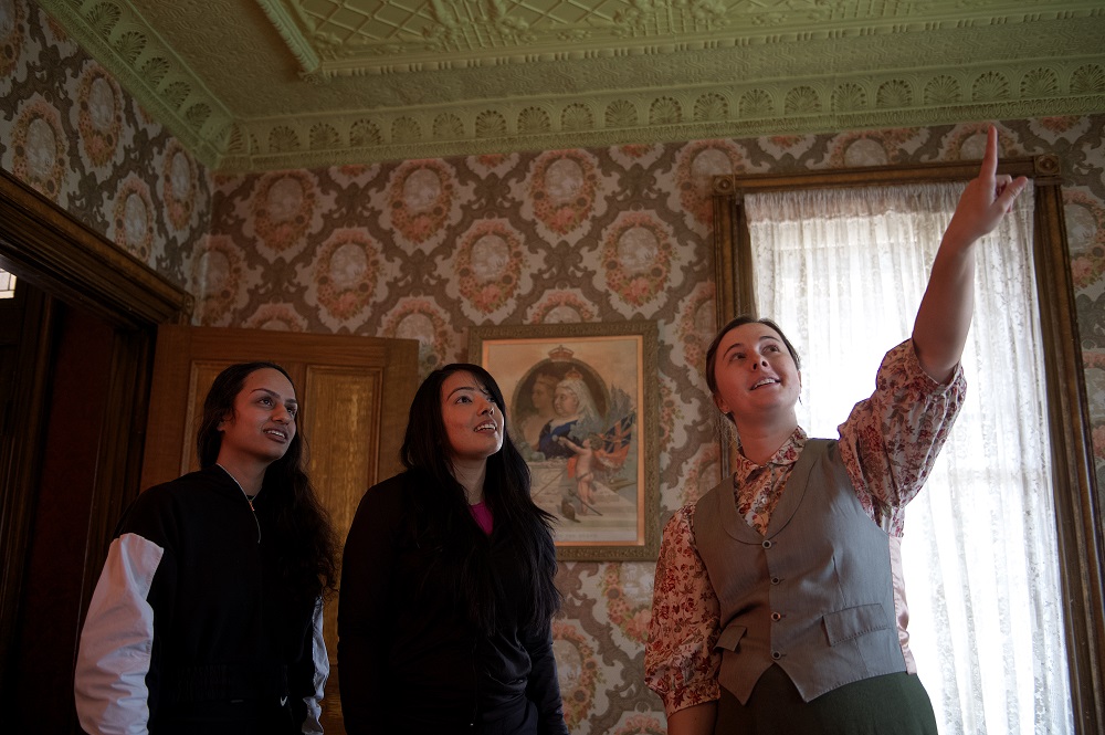 staff in victorian clothing pointing to ceiling with two visitors
