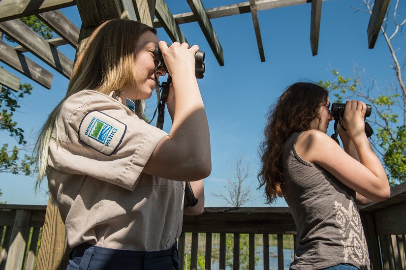 One park staff and one visitor look through binoculars.