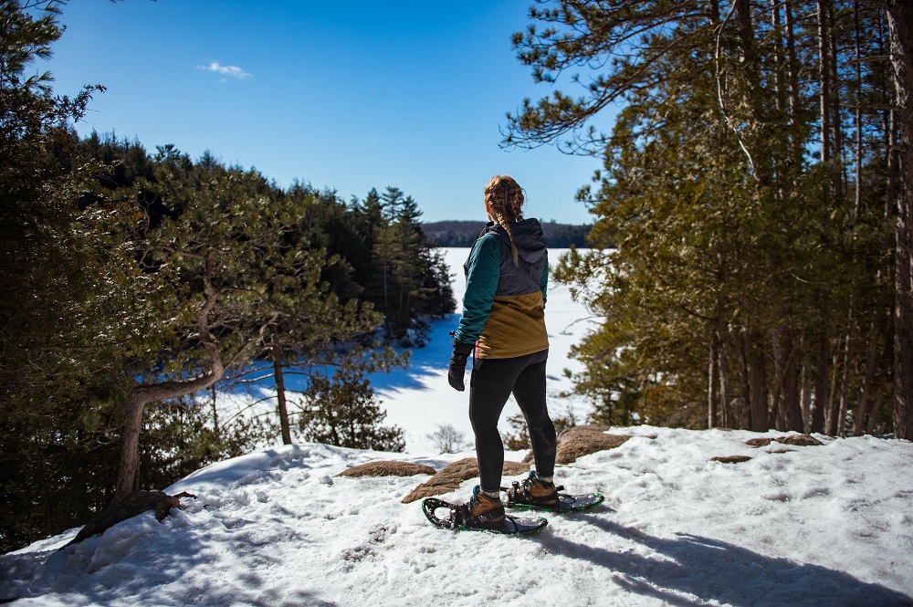 person in snowshoes, looking out at frozen lake