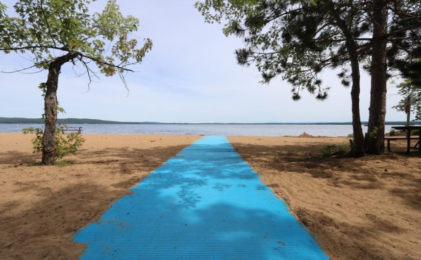 Large voie piétonnière bleu pâle menant à l’eau sur une plage de sable
