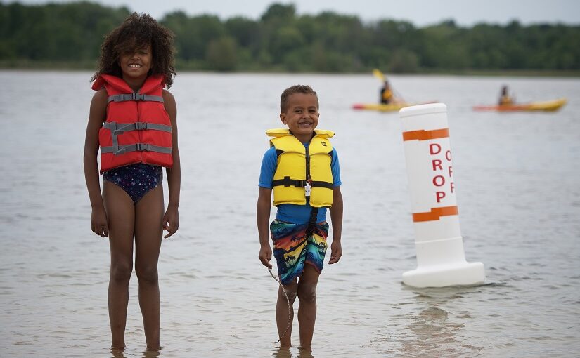 Children in lifejackets at water's edge.