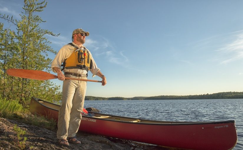 Man stands with paddle next to canoe