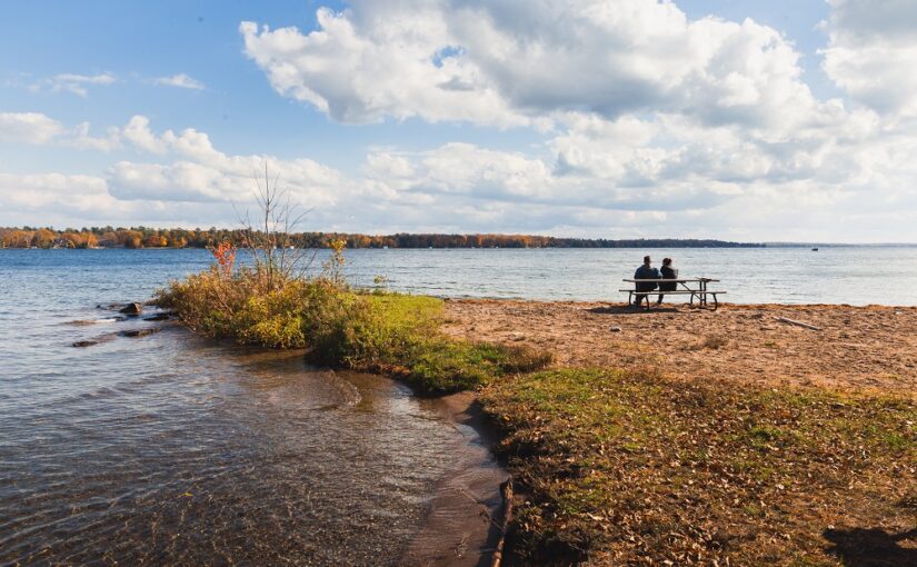 two people sitting on picnic bench looking out at water